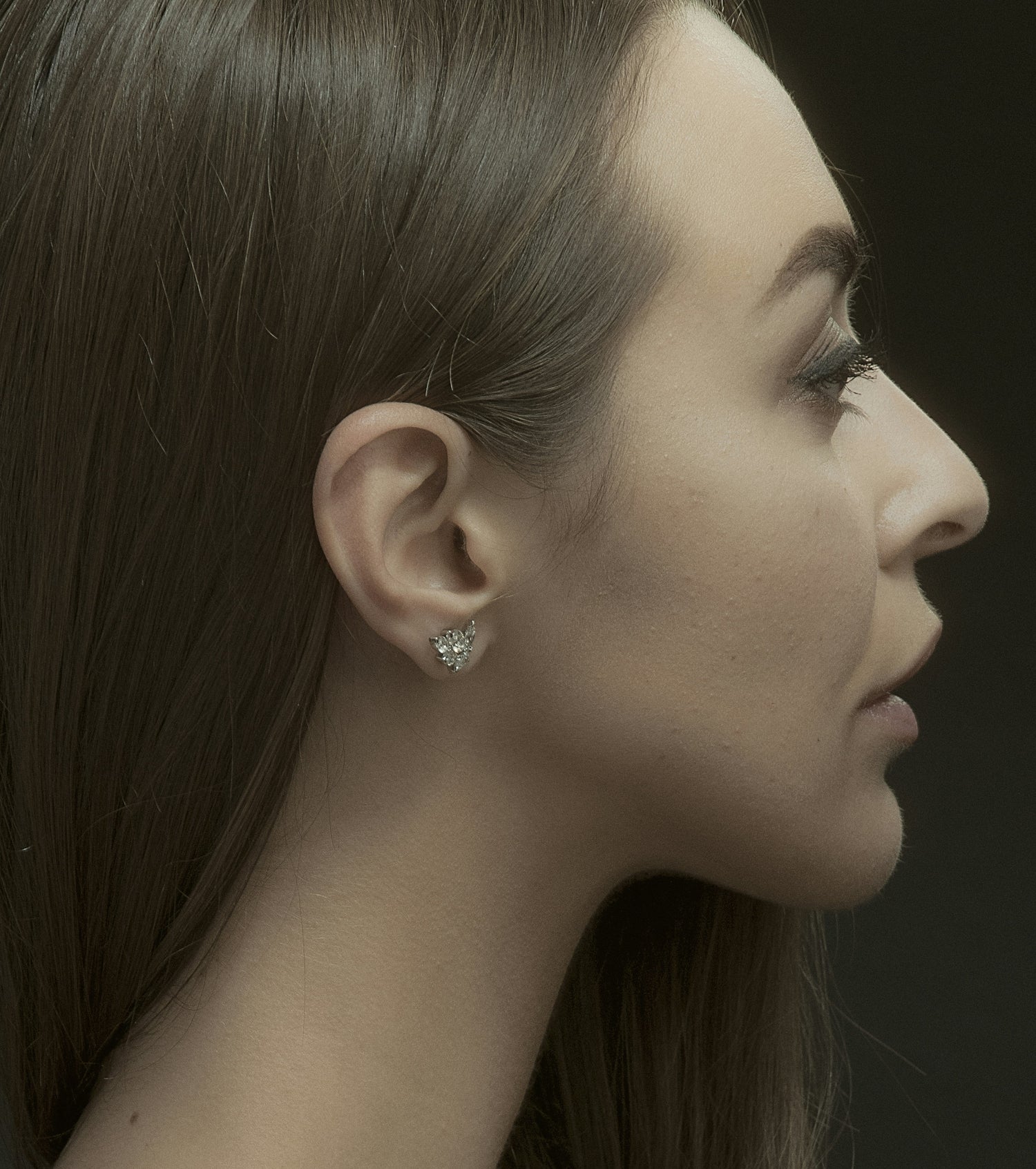 Side profile of a woman wearing a diamond earring against a dark background